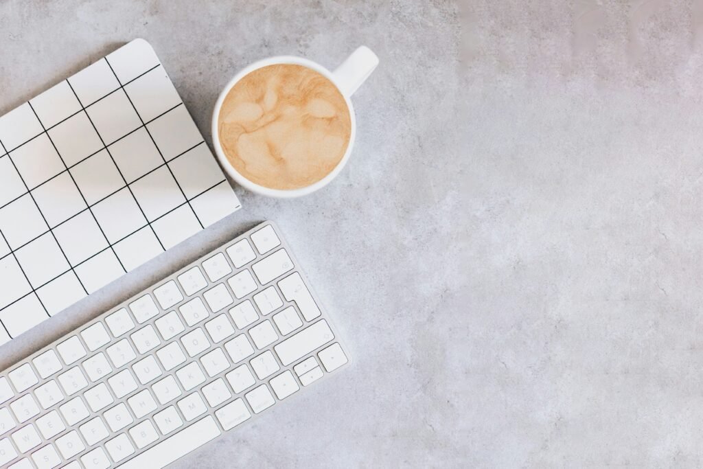 Top view of a workspace with a keyboard, a grid notebook, and a cup of coffee on a gray desk