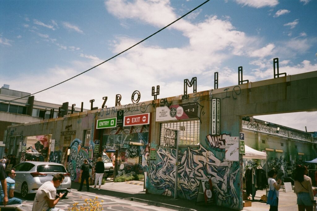 People exploring an urban market area at Fitzroy Mills with graffiti-covered walls and a vibrant atmosphere.