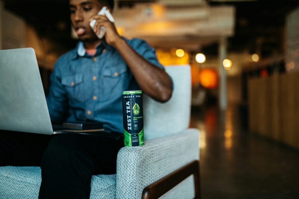 Person in a casual office setting using a laptop and phone with a Zest Tea energy drink on the armrest