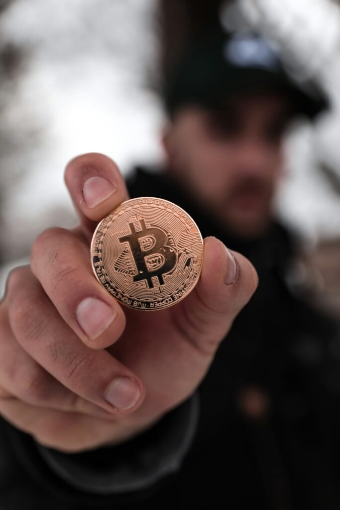 Hand holding a Bitcoin coin in focus, representing cryptocurrency investment.