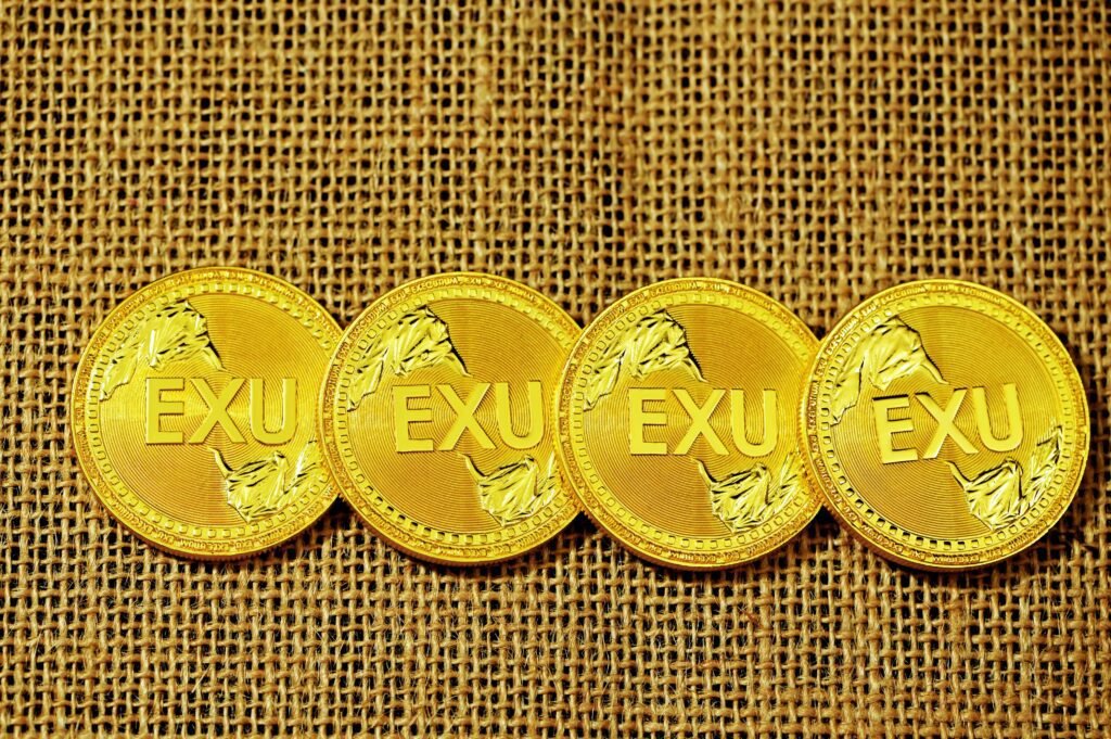 Four gold EXU coins displayed on a textured brown surface.