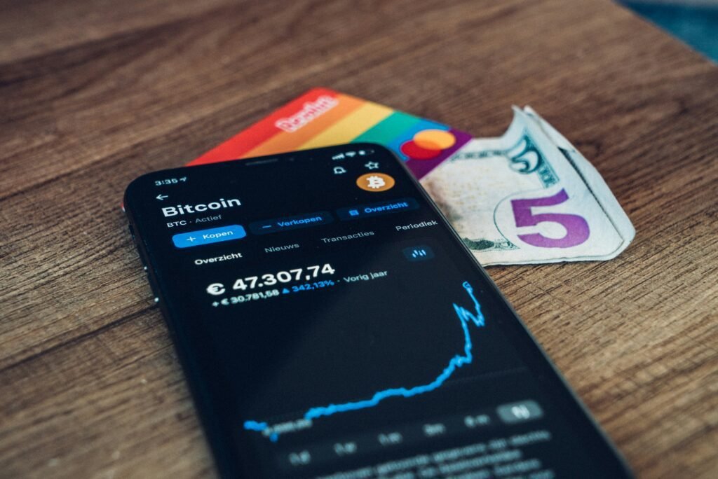 Smartphone displaying Bitcoin price chart next to a credit card and currency notes on a table.