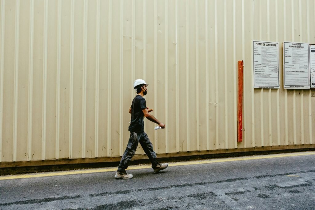 Construction worker walking past a building site with planning permits displayed on the wall