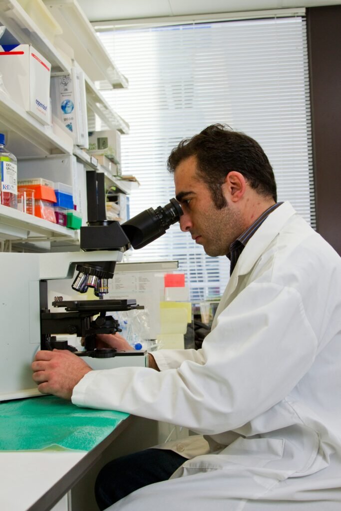 Scientist in a lab coat looking through a microscope in a laboratory setting.