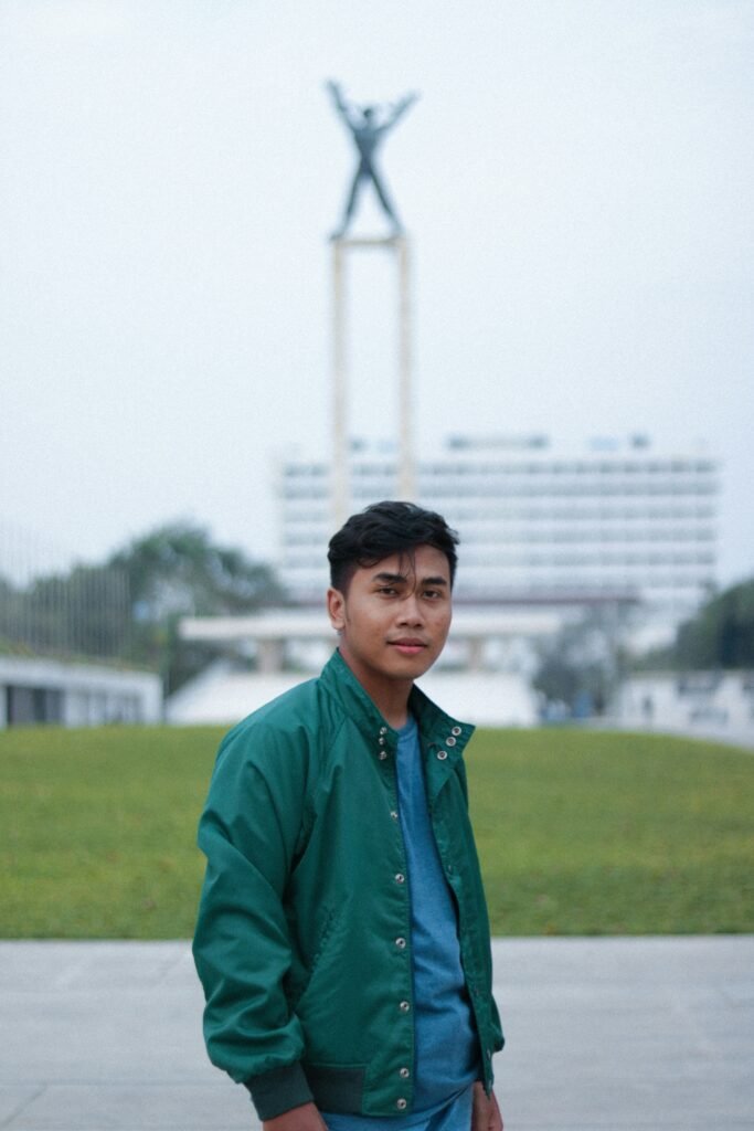 Young man standing in front of a monument with arms raised, symbolizing triumph and progress.