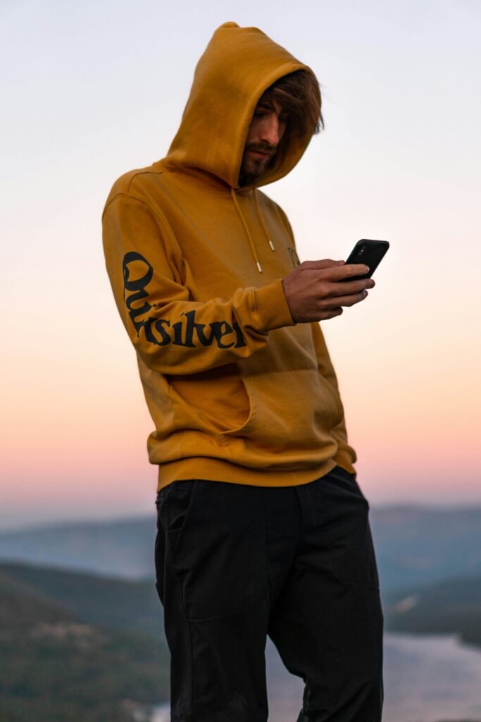 Person in a yellow hoodie looking at a smartphone at sunrise, symbolizing crypto market monitoring