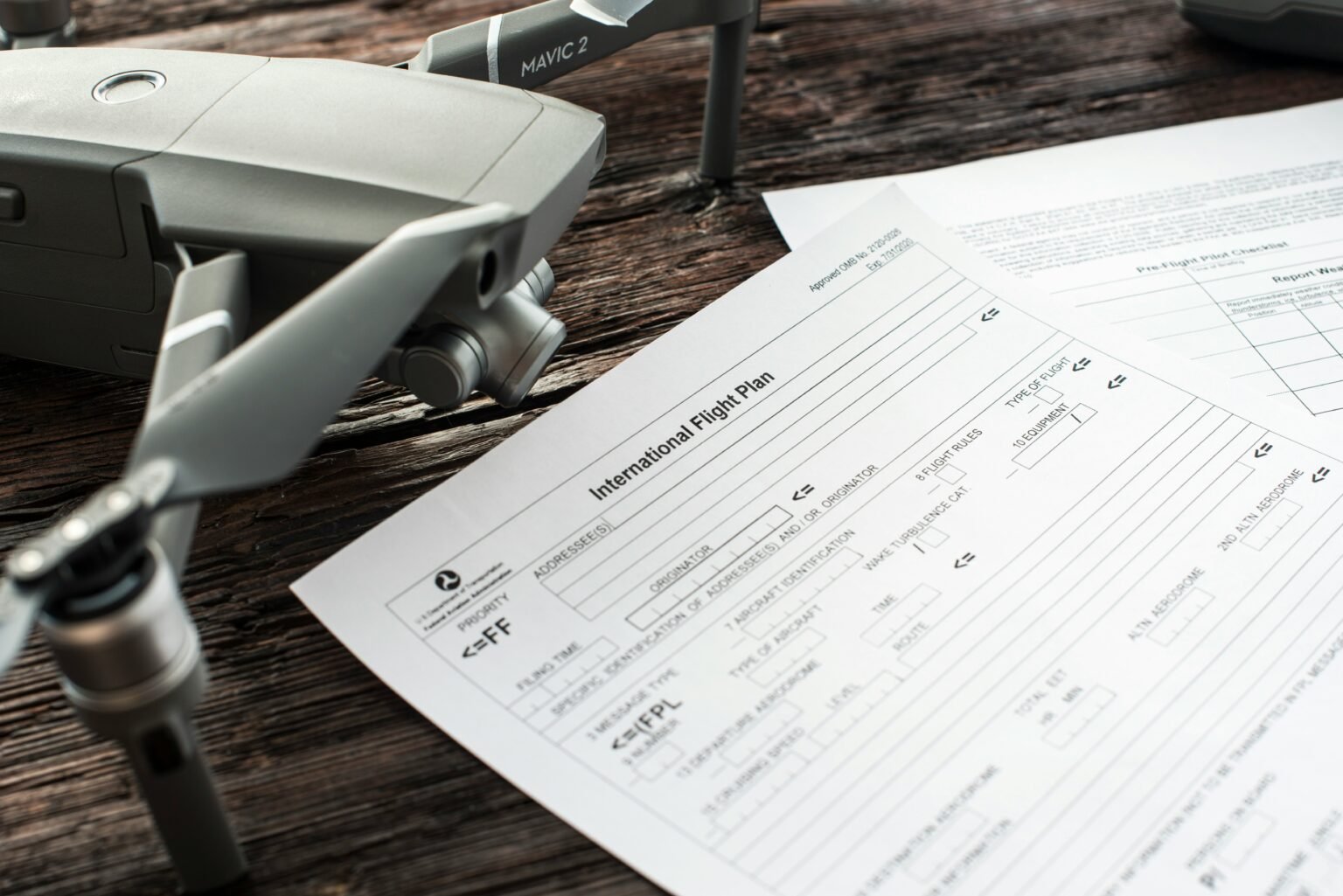 Close-up of a drone and an international flight plan document on a wooden table.